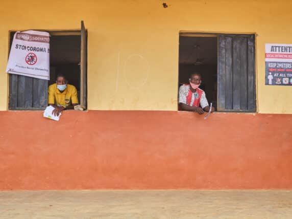 Two men look though windows with covid awareness signs