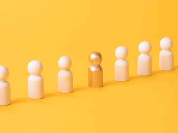 Row of wooden figurines with one gold figurine on yellow background