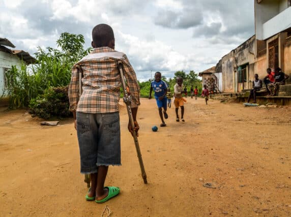 : A child, Zambo, who has a physical impairment, watches his friends play at a Sightsavers supported inclusive school in Cameroon.